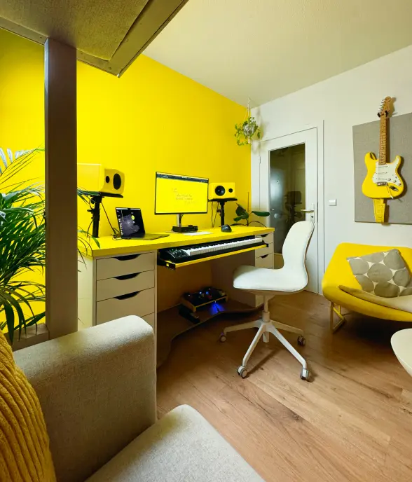 Studio room with yellow desk, monitors and a guitar mounted on the wall